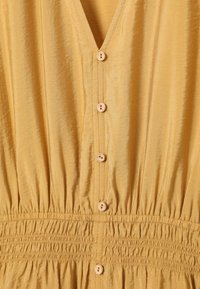 Robe en tissu jaune avec des boutons en bois au centre et une taille élastiquée froncée sous les boutons.