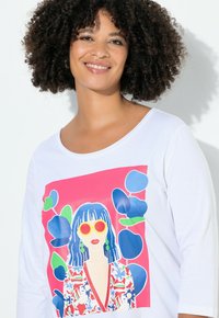 Witte T-shirt met een kleurrijke grafische print van een vrouw met blauw haar en zonnebril, omringd door groene en blauwe bloemelementen.