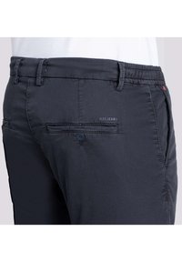 Dunkelblaue Hosen aus leichtem Stoff. Sie verfügen über einen Knopfverschluss, Gürtelschlaufen und eine Gesäßtasche mit einem dezenten Logo und einem einzelnen Knopfdetail.