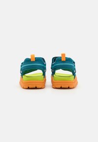 Tealmønstrede sandaler med oransje gummisåler og justerbare stropper. Har en grønn polstret såle og en bakre trekkertab for enkel påkledning.