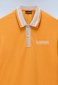 Orange polo t-shirt i tekstureret stof med en beige krave med hvide striber. Indeholder to knapper og broderet logo på brystet.