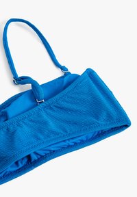Blå bikini top med tekstureret stof, justerbare stropper og metal hardware-detaljer. Har et sømløst design for komfort og pasform.