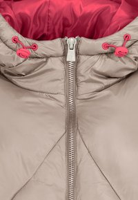 Beige gepolsterte Jacke mit rotem Innenfutter, ausgestattet mit einem metallischen Reißverschluss und verstellbaren Kordelzügen an der Kapuze mit rosafarbenen Akzenten.