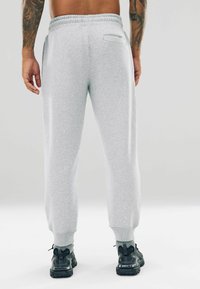 Grijze sweatpants met een elastische tailleband, taps toelopende pijpen en ribbenboorden. Voorzien van een enkele achterzak. Gecombineerd met zwarte sportschoenen.