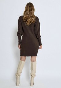 Brown knitted sweater dress with ribbed cuffs and hem, paired with knee-high beige boots. Smooth texture, form-fitting silhouette.