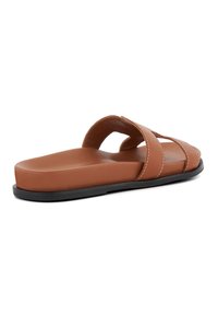 Bruine slide sandaal met twee gekruiste banden, platte zool en een zwarte rubberen basis. Gladde textuur met contrasterende witte stiksels.