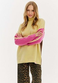 Pletený sveter v svetložltej farbe s rukávmi v ružovej a hnedej farbe v štýle farebných blokov. Spárované s čiernymi a hnedými nohavicami s leopardím vzorom. Mäkko-textúrovaný.