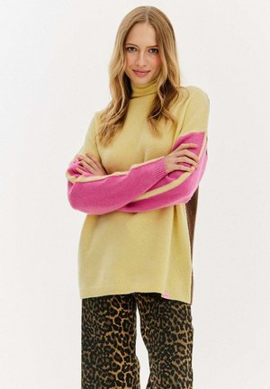 Sweter dziewiarski w jasnym żółtym kolorze z różowymi i brązowymi rękawami w stylu color-block. Połączony z czarnymi i brązowymi spodniami w panterkę. Miękka tekstura.