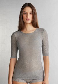 Haut gris à côtes avec des manches courtes, fabriqué dans un tissu semi-transparent. Il présente un col rond et une coupe slim.