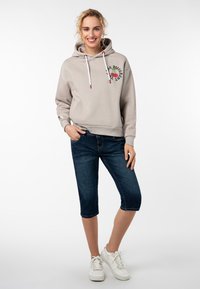 Lichtgrijze hoodie met een print aan de voorkant, witte trekkoorden, gecombineerd met donkere denim bermuda shorts en witte sneakers.