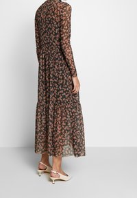 Schwarzes Blumen-Maxikleid mit langen Ärmeln, mit einem rüschierten Saum und leichtem, transparentem Stoff. Tragen mit cremefarbenen Slingback-High Heels.