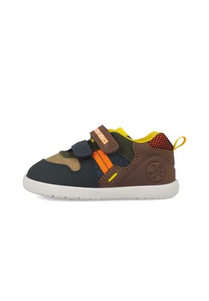 Zapatilla multicolor para niño pequeño con detalles en marrón, azul marino, naranja y amarillo, dos tiras de velcro y una suela de goma blanca.