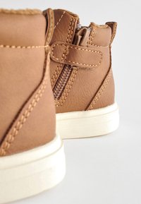 Bruine leren enkelboots met een gestructureerde afwerking, voorzien van een zijrits en contrasterende stiksels, gezet op een witte rubberen zool.
