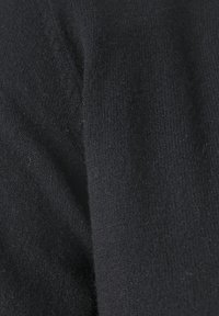 Detailní záběr černé pletené látky ukazující texturované vlněné vlákna a těsné šicí vzory.