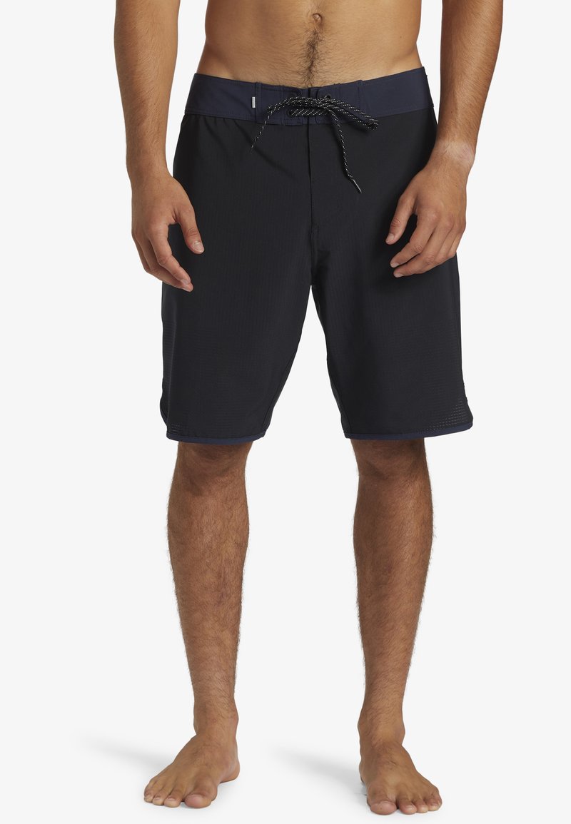 Shorts de bain noirs avec une ceinture bleu marine, fermeture à cordon de serrage et tissu texturé ; longueur genou avec un ourlet plat.