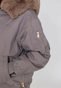 Graue Bomberjacke mit einem Kunstfellkragen, Reißverschlusstasche am Ärmel und gerippten Bündchen. Verfügt über goldene Hardware und ein leichtes Material.