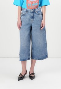 Svetlo modri denim culottes z udobnim krojem, z medsešnjim pasom, sprednjimi žepi in surovim robom. Ujemajo se z črnimi čevlji z ostrimi prsti.