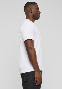 Hvid bomulds T-shirt med rund hals og korte ærmer, vist fra siden. Materialet ser glat og let tætsiddende ud.