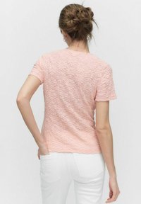 Rosa kortærmet t-shirt med et struktureret mønster, en tætsiddende pasform og en rund halsudskæring, parret med hvide jeans.