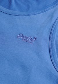 Top sin mangas de algodón azul con un escote redondeado y un pequeño logotipo bordado. Textura suave con costuras cosidas y sin patrones.