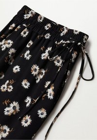 Pantalon en tissu noir avec imprimé floral de marguerites blanches et brunes, taille élastique et cordon de serrage assorti.