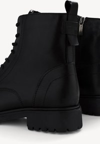 Bottines en cuir noir avec une finition texturée, dotées d'un laçage à l'avant, d'une fermeture éclair sur le côté et d'une semelle en caoutchouc durable avec un motif cranté.