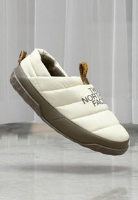 Fehér szigetelt slip-on cipők párnázott dizájnnal, texturált barna talppal, és színes szőtt részletekkel a hátsó részen. Az oldalon logó található.