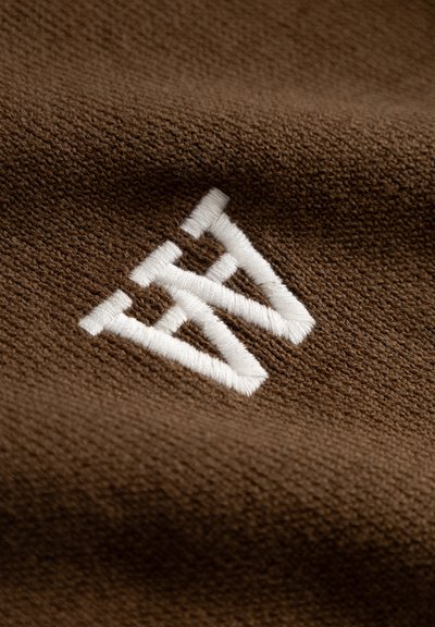Tissu marron avec un tissage texturé comportant un logo brodé blanc ressemblant à des triangles imbriqués.