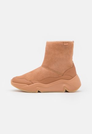Bottine en daim couleur beige moyen avec semelle en caoutchouc épaisse à motif ondulé et détails en cuir lisse au talon et à l'avant.