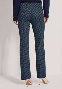 Vrouw in rechte marineblauwe broek met een klein blauw bladmotief, gecombineerd met beige hoge hakken en een donkere trui.