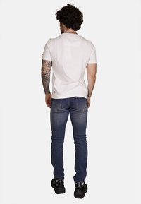 T-shirt bianco a maniche corte abbinato a jeans di denim blu. I jeans hanno un design aderente e sono indossati con scarpe da ginnastica nere.