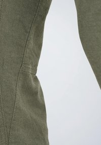 Prenda de algodón verde con un acabado texturizado, que presenta costuras cosidas y un bolsillo lateral. La tela parece suave y transpirable.