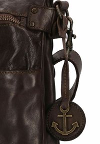 Borsa in cuoio marrone scuro con zip in ottone e un charm a forma di ancora in metallo attaccato da una cintura di pelle e un gancio in metallo.