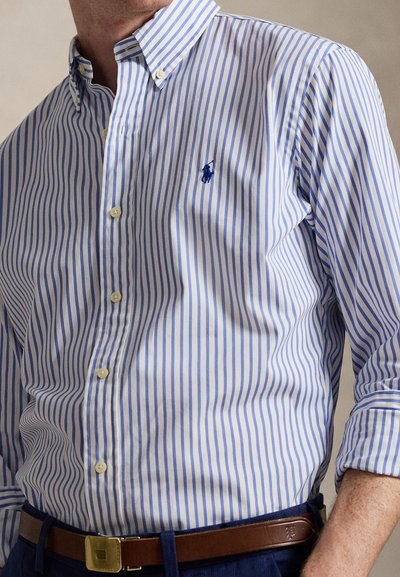 Button-down shirt with blue and white vertical stripes, featuring a small embroidered logo, and paired with a brown belt.