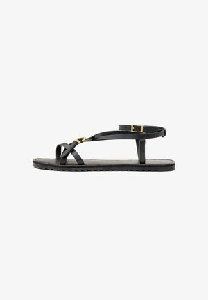 Zwarte leren sandalen met dunne banden en een gespsluiting rond de enkel. Platte zool met een gestructureerde afwerking en een zigzagrand. Minimalistisch design.