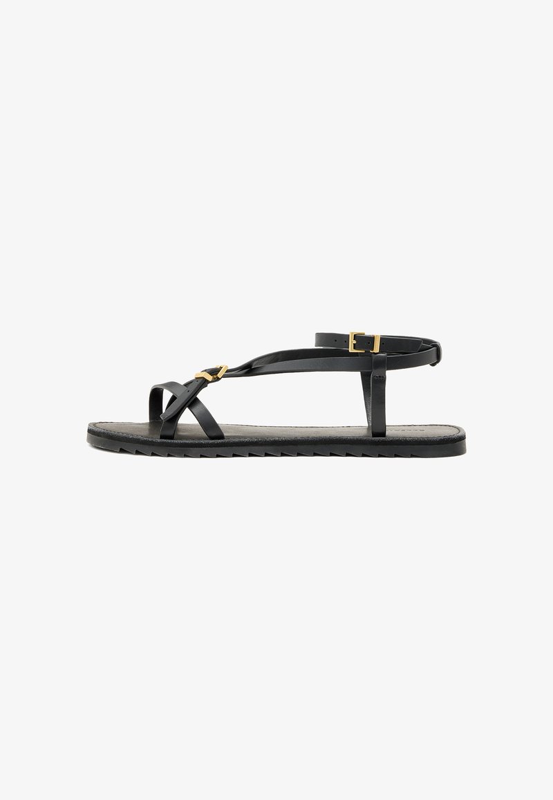 Sandálias de couro pretas com tiras finas e uma faixa no tornozelo com fivela. Sola plana com um acabamento texturizado e borda em zigzag. Design minimalista.