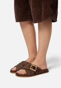 Brune vævede slidesandaler har et krydsbåndedesign med en struktureret finish og en guldfarvet spændeaccent på siden.