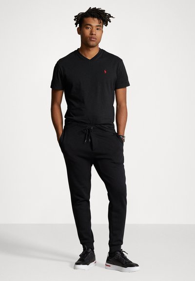 Black cotton v-neck t-shirt with red polo logo, paired with black jogger pants featuring drawstring waist and side pockets, completed with black sneakers.