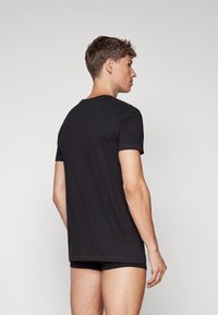 Svart bomull t-skjorte med korte ermer, rund halslinning, og en glatt tekstur, iført med svarte shorts, sett fra baksiden.