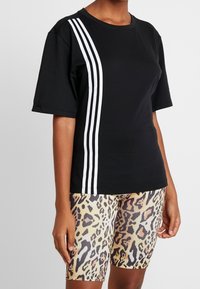 Czarny t-shirt z krótkim rękawem z trzema białymi paskami po jednej stronie, w połączeniu z szortami rowerowymi w panterkę, ukazującymi teksturowe wzory.