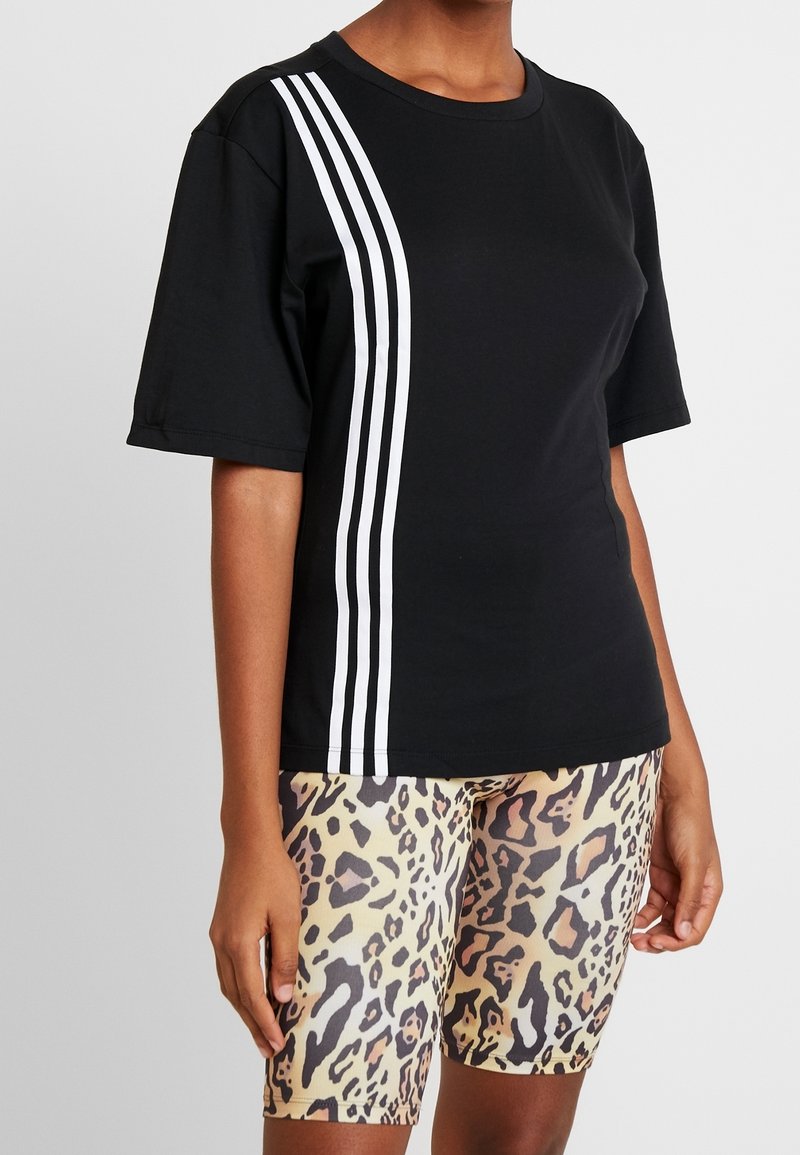 Czarny t-shirt z krótkim rękawem z trzema białymi paskami po jednej stronie, w połączeniu z szortami rowerowymi w panterkę, ukazującymi teksturowe wzory.