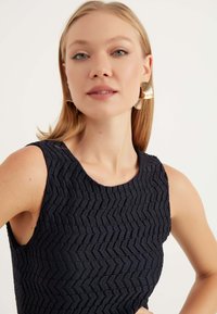 Un vestito di colore blu navy con una texture e un motivo geometrico, caratterizzato da un scollo arrotondato e senza maniche, abbinato a grandi orecchini dorati.