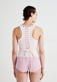 Top din material roz deschis, cu spate cu șnur și ochiuri metalice, asociat cu pantaloni scurți roz deschis cu textură canelată. Design ajustat cu textură moale.