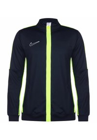 Nike jack in marineblauw met een felgele rits. Heeft een hoge kraag, lange mouwen en een wit logo aan de linkerkant. Soepele stof.