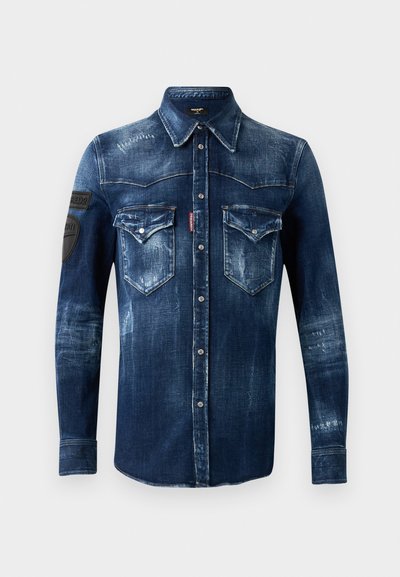 Dunkelblaues Denim-Hemd mit langen Ärmeln, Knopfleiste, zwei Taschen mit Klappen auf der Brust und abgegriffenen Details, mit schwarzen Patches auf dem linken Ärmel.