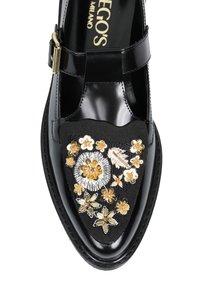 Czarny lakierowany but z paskiem T, z misternymi haftami kwiatowymi w kolorze złotym, białym i kremowym na czarnej tkaninie.