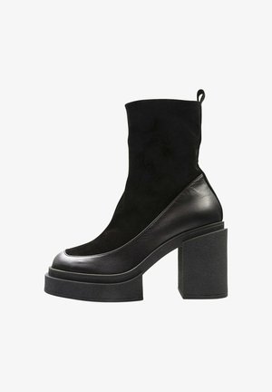 Botín negro con una combinación de materiales de cuero y ante, puntera redondeada y un grueso tacón de bloque texturizado.