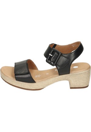 Sandale en cuir noir avec une large lanière, une boucle ajustable et un talon compensé clair texturé. Semelle intérieure lisse avec un bout arrondi.
