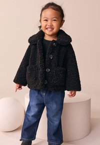 Black, textured fleece jacket with a wide collar, four buttons, and two front pockets, paired with blue denim jeans in a neutral background.