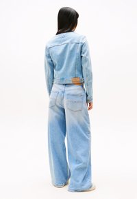 Giacca di jeans azzurro chiaro con un design leggermente accorciato e jeans a gamba larga coordinati. Presenta cuciture classiche, due tasche posteriori e etichetta con il marchio.